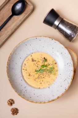 Bir tabak peynirli, fındıklı, yeşillikli ve arka planda bej bir krem çorba.