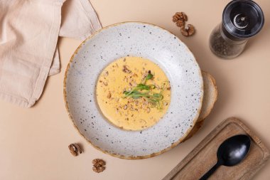 Bir tabak peynirli, fındıklı, yeşillikli ve arka planda bej bir krem çorba.