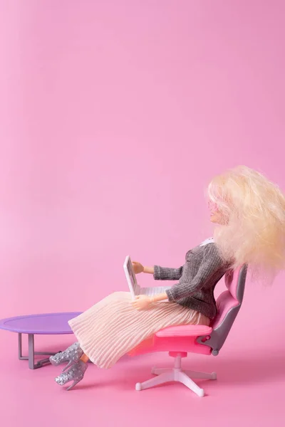 Doll with laptop in chair on pink background. Working at home, freelance creative concept