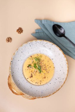 Bir tabak peynirli, fındıklı, yeşillikli ve arka planda bej bir krem çorba.