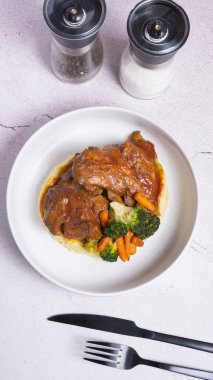 Kırmızı soslu bir tabak biftek, sebzeli ve patates püresi ve siyah çatal bıçak..