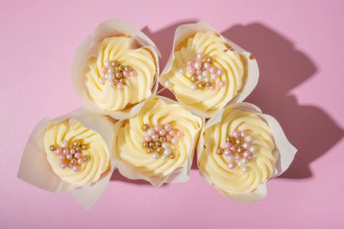 Tatlı tatlı beş kek kremalı ve inci desenli pembe arka plan manzaralı, düz uzanmış.