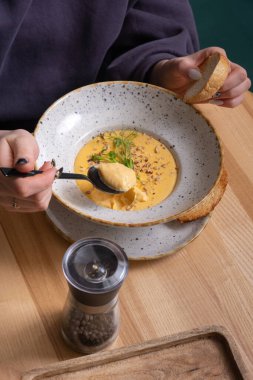 Elinde bir tabak krem peynirli, fındıklı ve sebzeli çorba olan bir kadının ellerinde bir kaşık..