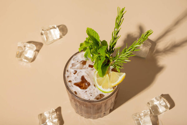 Alcoholic cocktail decoration mint, lime and lemon and ice cubes on a beige background top view, flat lay.