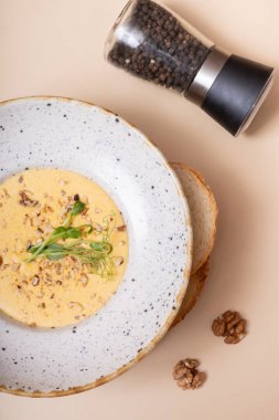 Bir tabak peynirli, fındıklı, yeşillikli ve arka planda bej bir krem çorba.