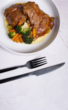 Kırmızı soslu biftek tabağı, sebzeli ve patates püresi ve siyah çatal bıçak..