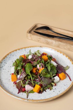 Sebzeli salata, balkabağı, yumuşak peynir ve bej arka planda çatal bıçak takımı..