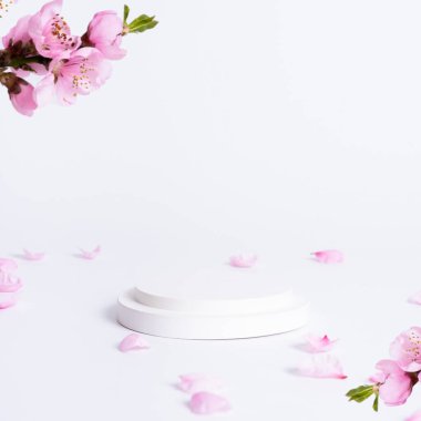 Beyaz odada pembe çiçekli bir podyum. Ürün sunum teması.