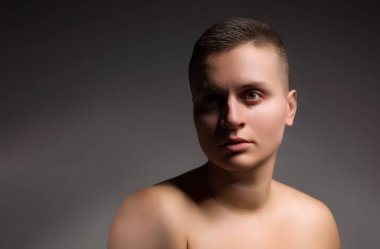 Gri arka planda kısa saçlı ve çıplak omuzlu genç bir kadının portresi.