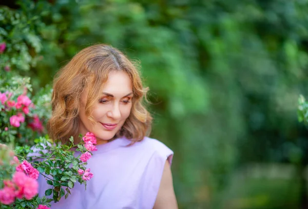 美丽而成功的中年妇女在户外的花园里嗅到了盛开的玫瑰的芬芳 街头摄影 免版税图库图片