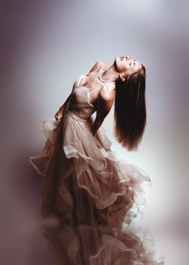 Şık ve zarif bir elbiseyle, zarif ve sanatsal bir şekilde poz veren çarpıcı bir kadın. Uzun saçları ve yumuşak kumaşı rüya gibi ve ruhani bir atmosfer yaratıyor. Saf güzelliği yakalıyor..