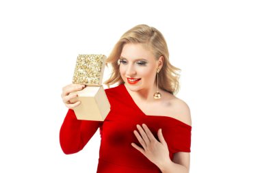 Kırmızı elbiseli ve altın küpeli zarif bir kadın elinde dekoratif bir hediye kutusu var. Onun sarı saçları ve kalın makyajı onun büyüleyici görünümünü güçlendirir. Tatil ve lüks kavramlar için mükemmel..