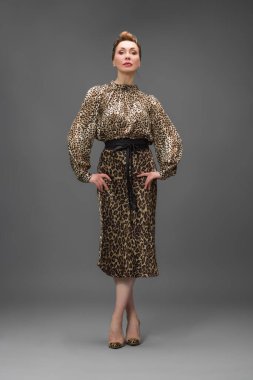 Leopar desenli elbisesi ve topuklu ayakkabısı olan zarif olgun bir kadın stüdyoda poz veriyor. Özgüven ve zarafetle şık moda portresi.