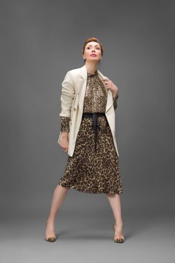 Leopar desenli elbisesi ve topuklu ayakkabısı olan zarif olgun bir kadın stüdyoda poz veriyor. Özgüven ve zarafetle şık moda portresi.