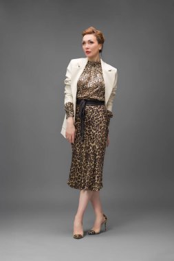 Leopar desenli elbisesi ve topuklu ayakkabısı olan zarif olgun bir kadın stüdyoda poz veriyor. Özgüven ve zarafetle şık moda portresi.