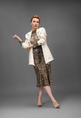 Leopar desenli elbisesi ve topuklu ayakkabısı olan zarif olgun bir kadın stüdyoda poz veriyor. Özgüven ve zarafetle şık moda portresi.
