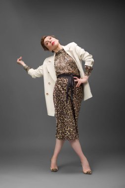Leopar desenli elbisesi ve topuklu ayakkabısı olan zarif olgun bir kadın stüdyoda poz veriyor. Özgüven ve zarafetle şık moda portresi.