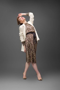 Leopar desenli elbisesi ve topuklu ayakkabısı olan zarif olgun bir kadın stüdyoda poz veriyor. Özgüven ve zarafetle şık moda portresi.