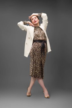 Leopar desenli elbisesi ve topuklu ayakkabısı olan zarif olgun bir kadın stüdyoda poz veriyor. Özgüven ve zarafetle şık moda portresi.