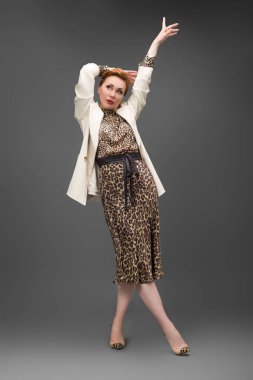 Leopar desenli elbisesi ve topuklu ayakkabısı olan zarif olgun bir kadın stüdyoda poz veriyor. Özgüven ve zarafetle şık moda portresi.