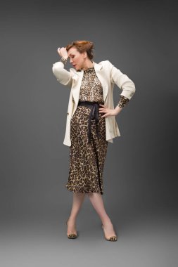 Leopar desenli elbisesi ve topuklu ayakkabısı olan zarif olgun bir kadın stüdyoda poz veriyor. Özgüven ve zarafetle şık moda portresi.