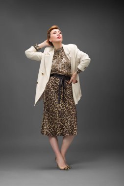 Leopar desenli elbisesi ve topuklu ayakkabısı olan zarif olgun bir kadın stüdyoda poz veriyor. Özgüven ve zarafetle şık moda portresi.