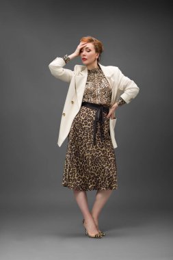 Leopar desenli elbisesi ve topuklu ayakkabısı olan zarif olgun bir kadın stüdyoda poz veriyor. Özgüven ve zarafetle şık moda portresi.