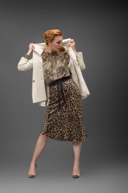 Leopar desenli elbisesi ve topuklu ayakkabısı olan zarif olgun bir kadın stüdyoda poz veriyor. Özgüven ve zarafetle şık moda portresi.