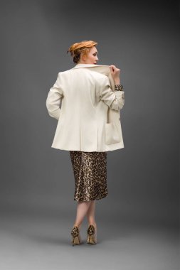 Leopar desenli elbisesi ve topuklu ayakkabısı olan zarif olgun bir kadın stüdyoda poz veriyor. Özgüven ve zarafetle şık moda portresi.