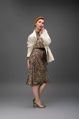 Leopar desenli elbisesi ve topuklu ayakkabısı olan zarif olgun bir kadın stüdyoda poz veriyor. Özgüven ve zarafetle şık moda portresi.