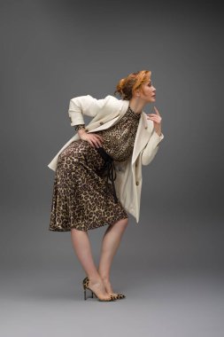Leopar desenli elbisesi ve topuklu ayakkabısı olan zarif olgun bir kadın stüdyoda poz veriyor. Özgüven ve zarafetle şık moda portresi.