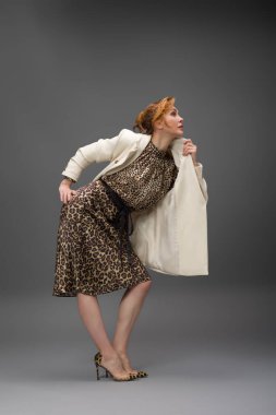 Leopar desenli elbisesi ve topuklu ayakkabısı olan zarif olgun bir kadın stüdyoda poz veriyor. Özgüven ve zarafetle şık moda portresi.