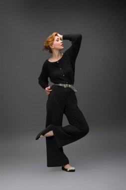 Siyah geniş paçalı pantolon ve kemerli bluz giyen zarif bir kadının moda portresi. Stüdyoda gri arka planda duruyor. Modern tarz ve kendine güvenen kadınsı görünüş.