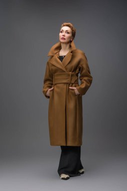 Uzun kahverengi kemerli zarif bir kadının moda portresi. Stüdyoda gri arka planda duruyor. Modern sonbahar tarzı ve kendinden emin kadınsı görünüş.
