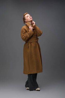 Uzun kahverengi kemerli zarif bir kadının moda portresi. Stüdyoda gri arka planda duruyor. Modern sonbahar tarzı ve kendinden emin kadınsı görünüş.
