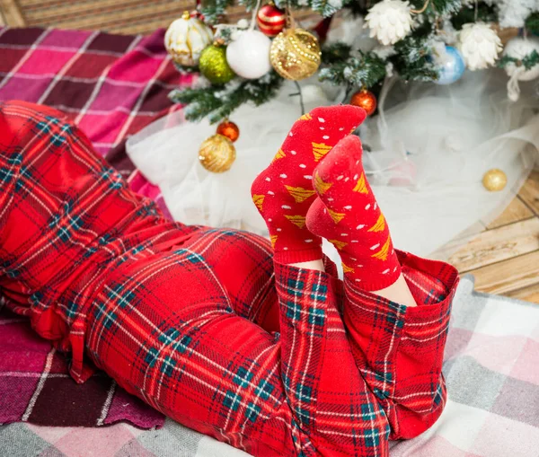 穿着节日睡衣躺在圣诞树旁的年轻女人 图库图片