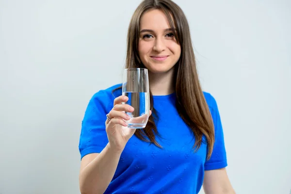 身穿蓝色衣服 面带微笑的年轻女子举着一杯晶莹清澈的水 准备喝水 — 图库照片