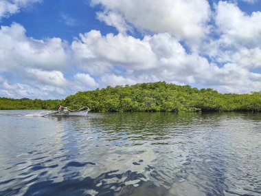 Siargao, Surigao, Filipinler - 11 Mart 2024: Erkekler bulutlar ve mangrov ormanlarından oluşan gerçeküstü bir manzaranın ortasında motorlu bir tekneye pilotluk yapıyor..