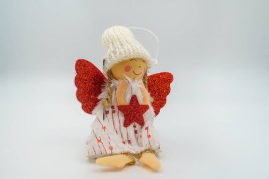 El yapımı Noel meleği bebeği, kırmızı parıltılı kanatlar, kırmızı yıldız, beyaz şapkayla süslenmiş, sarı iplik saçı, kalp desenli elbise, altın ayaklar, gülen tahta yüz. Beyaz arkaplan