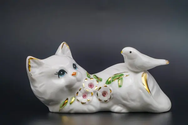 Porcelain playful cat, ceramic statuette. Dove, embellishment, petals and leaves gilded edges. Hand-painted refined. Shiny surface, collectible item. Graceful posture, handcrafted. Black background