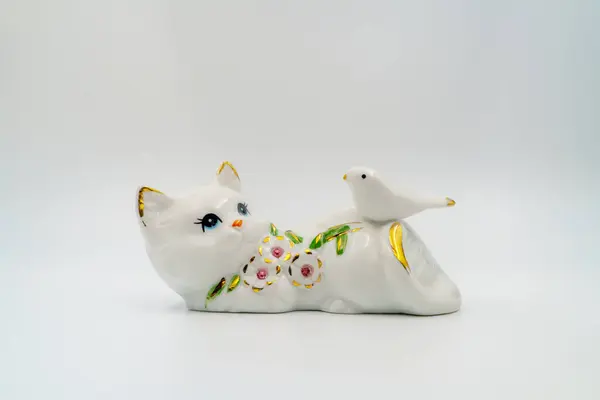 Ceramic statuette, porcelain playful cat. Dove, petals and leaves embellishment, gilded edges. Shiny surface, collectible item. Hand-painted refined. Graceful posture, handcrafted. Black background