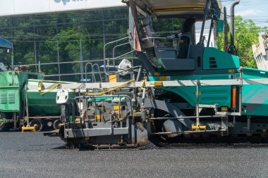 Asfalt hammer makinesi hazır yol yatağı üzerine sıcak bitumen karışımı yayar, ardından pürüzsüz yüzey bitimi için sıkıştırıcı, kentsel altyapı gelişimi ve otoyol geliştirme sürecini gösteren.