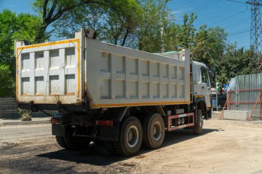 İnşaat alanına yerleştirilmiş çöp kamyonu yeniden yüzey, eskrim, elektrik direkleri ve inşaat bariyerleri için asfalt dağıtıyor, aktif kentsel altyapı iyileştirme projesini vurguluyor.