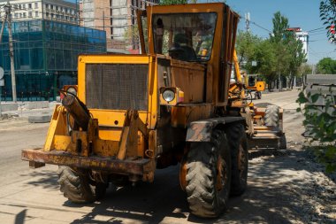 Grader şehir caddesinde çalışır, asfaltı düzleştirir ve yeni asfalt için düzleştirir. İnşaat ekipmanları, kentsel çevre ve devam eden yol çalışması altyapı geliştirme ve bakım çalışmalarını ön plana çıkardı.