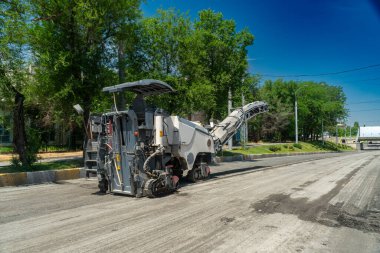 Ağır yol değirmeni ekipmanları yıpranmış asfalt yüzeyini öğütüyor ve kaldırıyor, yeni asfalt döşemeleri için yol hazırlıyor. Şehir altyapısı, inşaat süreci, makine operasyonu, ulaşım güncellemesi.