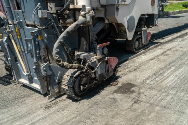 Rayların alt kısmına sahip ağır makineler, dönen davul öğütücüleri ve yıpranmış asfalt tabakasını kaldırıyor, yeniden yüzeye çıkmaya hazırlanıyor, yol dayanıklılığını artırıyor, ulaşım altyapısını yükseltiyor.