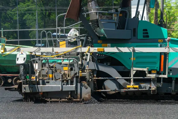 Asfalt kaldırım taşı, yeni yol için hazır yol yatağı, sıkıştırma ve düzleştirme yüzeyine sıcak bitumen karışımı yayar. İnşaat ekipmanları açık havada çalışır, araçlar için düzgün dayanıklı kaldırımlar sağlar..