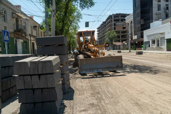 İnşaat makinesi seviyeleri asfalt döşeme için asfaltlanmamış yol yüzeyi. Yakınlarda beton kaldırım taşları var. Kentsel çevre, binalar, altyapı güncellemesi.
