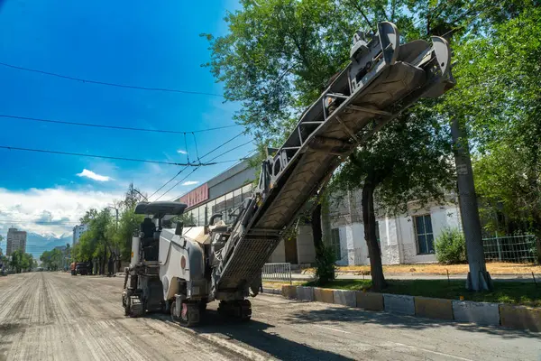 Yıpranmış yol yüzeyini ağaçlar, kaldırımlar ve kentsel altyapı ile çevrili yeni kaldırımlar için öğütüyor ve kaldırımları kaldırıyor..