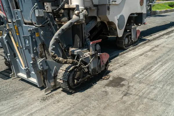 Rayların alt kısmına sahip ağır makineler, dönen davul öğütücüleri ve yıpranmış asfalt tabakasını kaldırıyor, yeniden yüzeye çıkmaya hazırlanıyor, yol dayanıklılığını artırıyor, ulaşım altyapısını yükseltiyor.